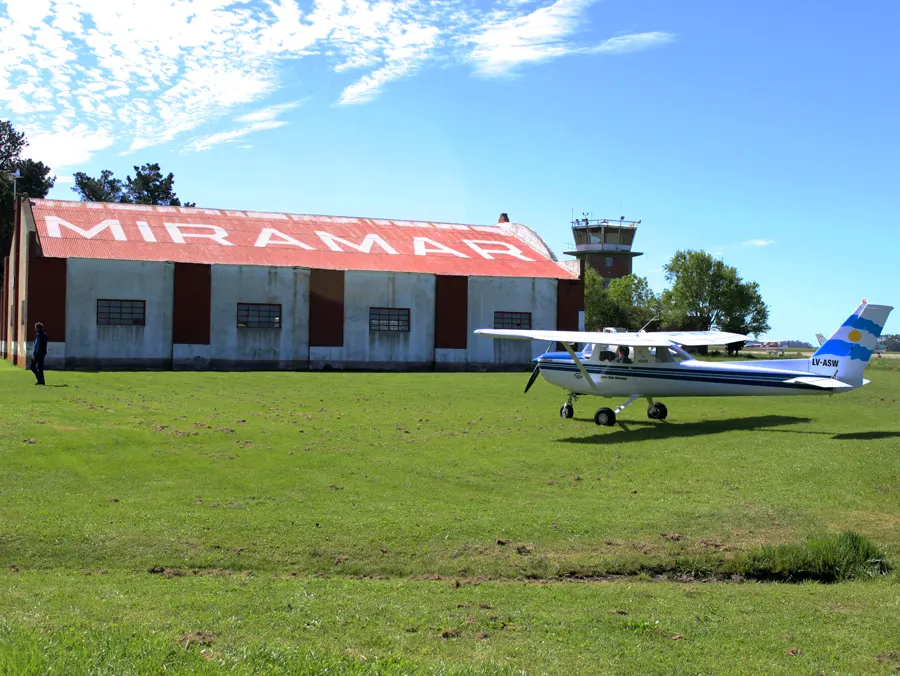 El hangar grande con el techo de chapa roja y la palabra MIRAMAR en letras blancas, con la torre de control detrás