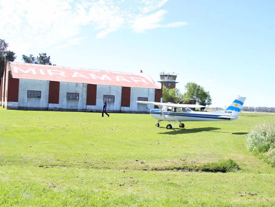 La torre de control de ladrillo con su cabina vidriada, detrás del hangar, y una Cessna con la bandera argentina en la cola
