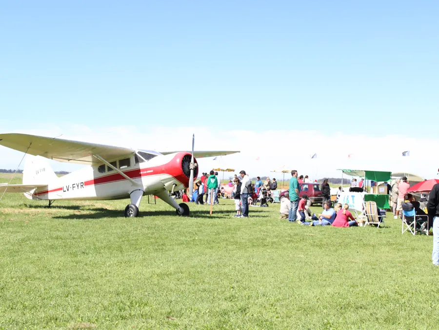 El Stinson Reliant LV-FYR, rojo y blanco, durante un encuentro en el aeródromo con familias sentadas en el pasto