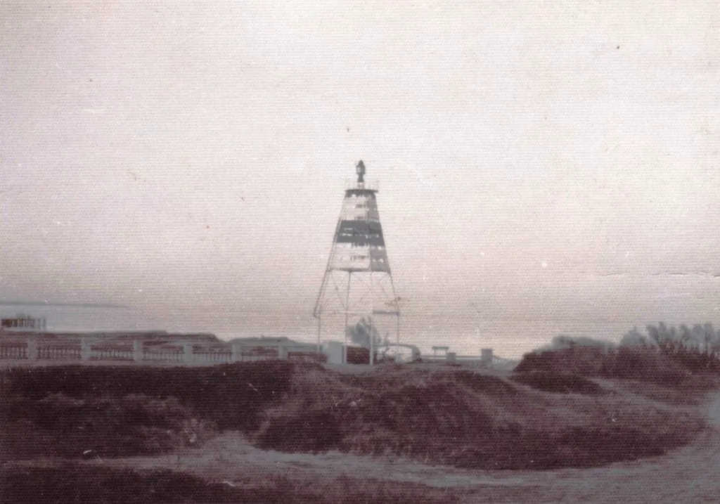 Foto antigua de la baliza con su marca de franjas, detrás de los pilares y el cerco de la entrada del vivero