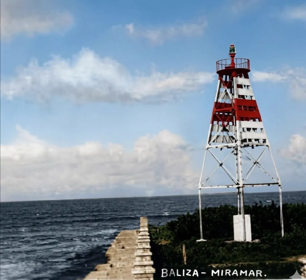 Foto coloreada de la baliza, con tablas rojas y blancas, una linterna chica arriba y el mar de fondo, con el cartel Baliza Miramar