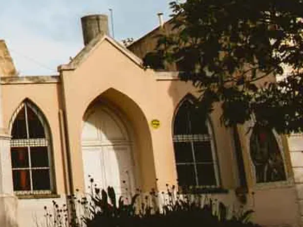 La nave lateral: un pórtico en punta con puerta blanca entre dos ventanas ojivales con rejas