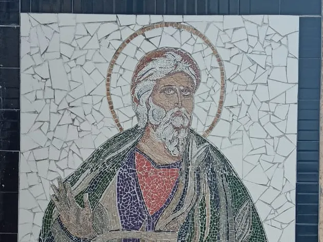 Mosaico de San Andrés Apóstol: el santo de barba blanca con aureola, túnica roja y violeta y manto verde, sobre un fondo de azulejos blancos partidos y un marco de azulejos negros