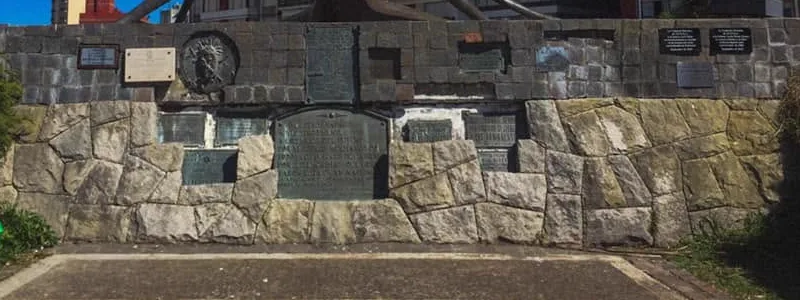 La pared de piedra de la base, con placas de distintos tamaños y un medallón con un rostro