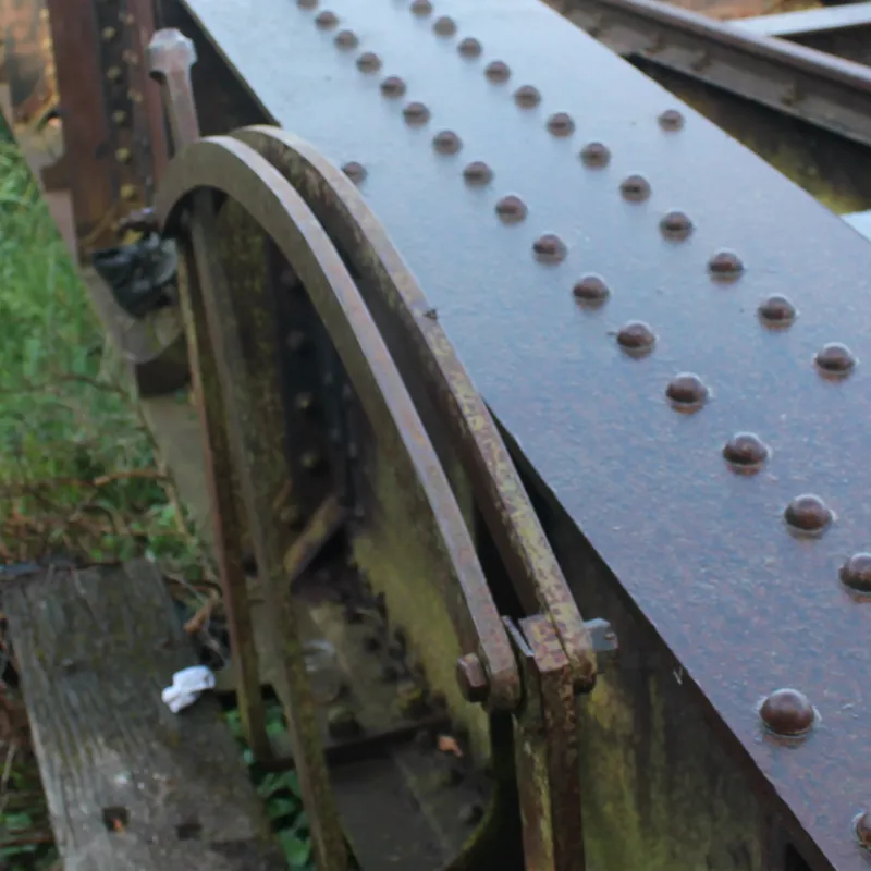 Detalle de la punta de una viga del puente: dos arcos de hierro sujetos con un perno, junto a las cabezas de los remaches
