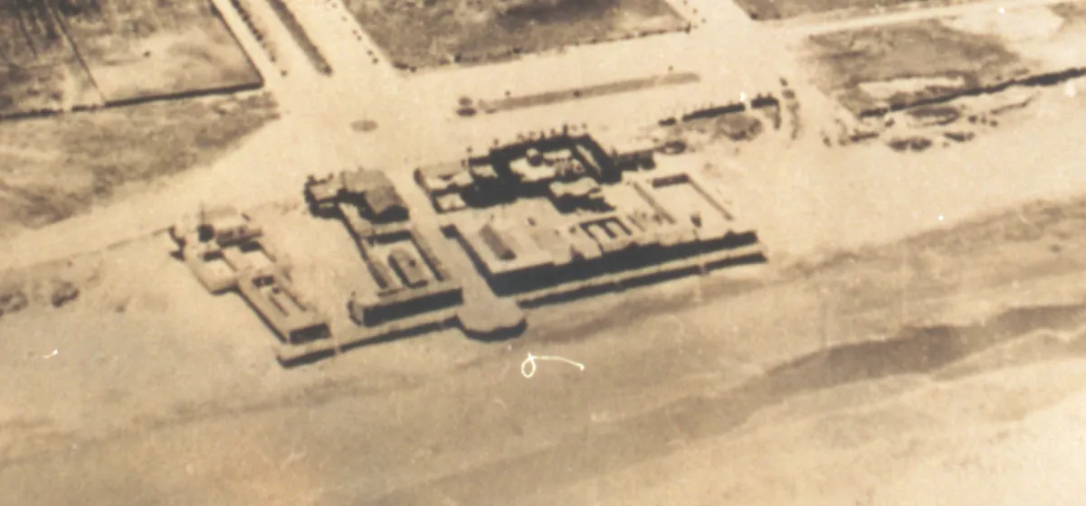 Vista aérea antigua de la rambla de hormigón sobre la playa, con varios cuerpos de edificios, patios y un saliente redondeado al frente