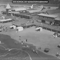 La rambla de madera vista desde lo alto, con la torre, los pabellones, el paseo con baranda y carpas en la arena