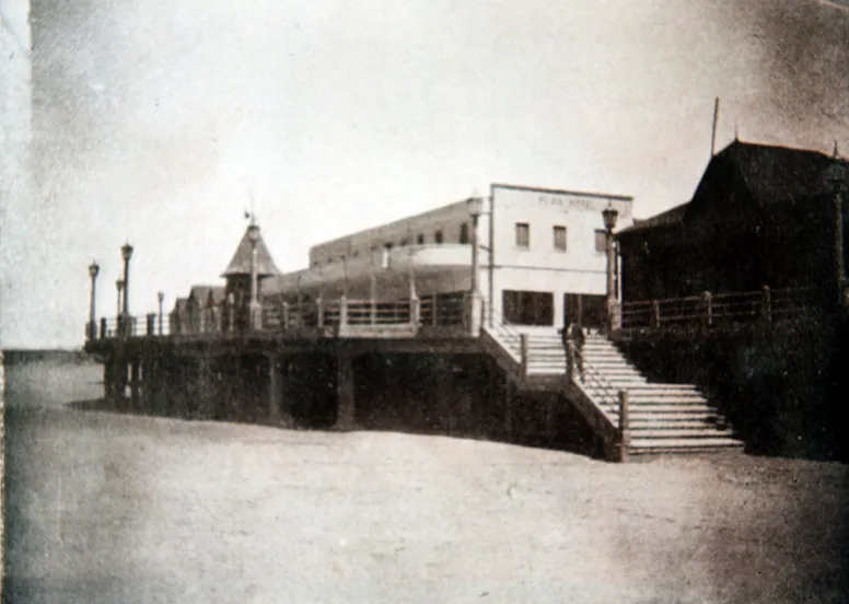 El Playa Hotel, de dos pisos y paredes blancas, sobre la plataforma de hormigón con faroles y una escalera ancha que baja a la arena