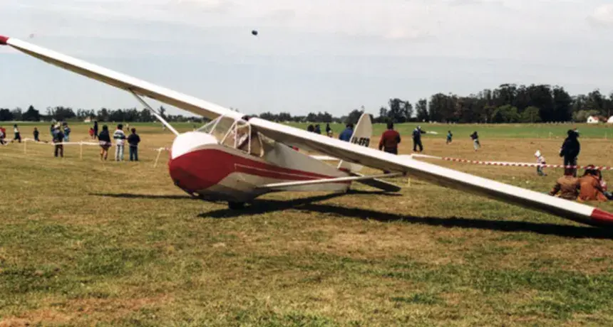 El planeador biplaza del aeroclub, rojo y blanco, apoyado sobre el pasto con gente alrededor